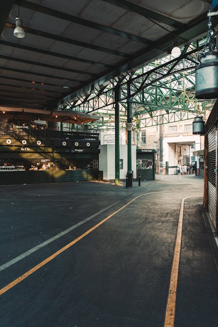 A covered loading area at Bermondsey Wharf with a high, dark metal roof supported by green and black structural beams, providing shelter for the furniture transport and packing process during home rel